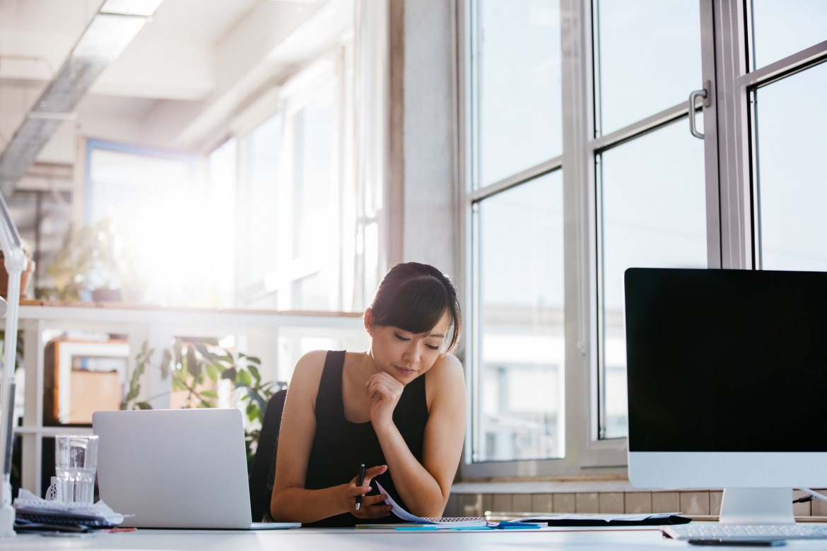 Woman looking at notebook and holding a pen while working on recruiting automation in her office next to a white laptop